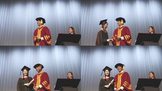 毕业典礼激动的亚洲毕业大学女学生在礼堂的舞台上接过毕业奖状后，举起手臂站在院长身边