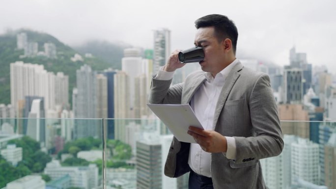 年轻的商人独自站在外面，用着平板电脑，背景是香港岛的建筑。