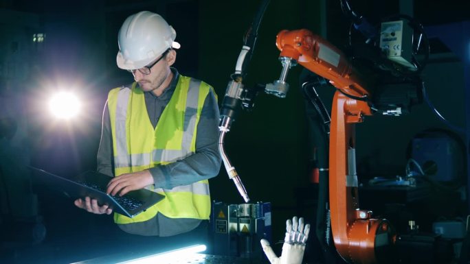 穿着安全服的男研究员正在观察一个机器人装置——仿生手臂。
