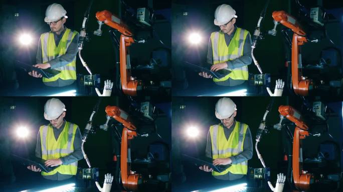 穿着安全服的男研究员正在观察一个机器人装置——仿生手臂。