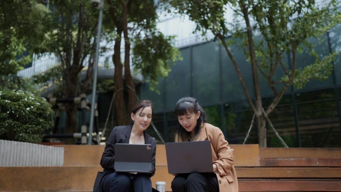 亚洲女同事坐在花园里，用笔记本电脑做在线项目，在办公室外进行头脑风暴。