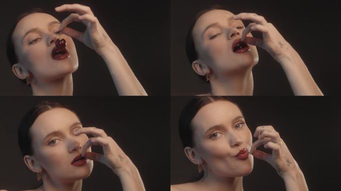 美丽的性感女人用红色的口红黑色的背景工作室拍摄咬一口樱桃水果和品尝