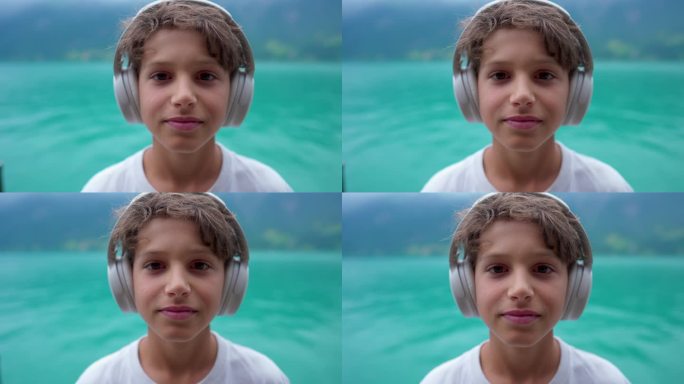 一个戴着耳机的小男孩站在湖边的画像。英俊的男孩一边听音频、播客、音乐或有声读物，一边看着镜头