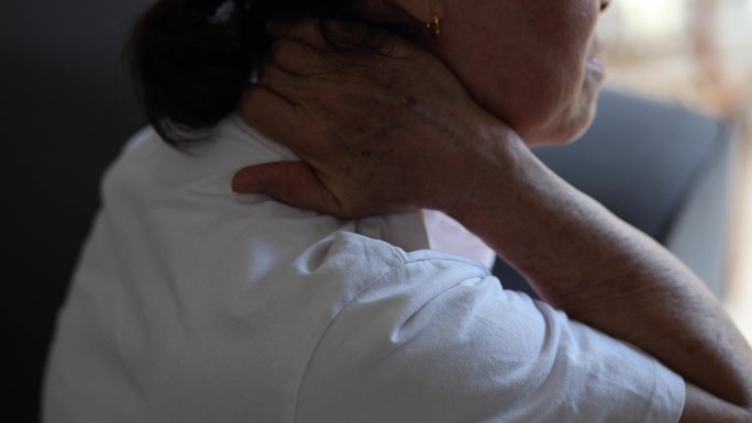 一位年长的亚洲女性在家里遭受脖子和肩膀疼痛的折磨。这种不适可能是由于压力、抑郁或睡眠不足等因素造成的