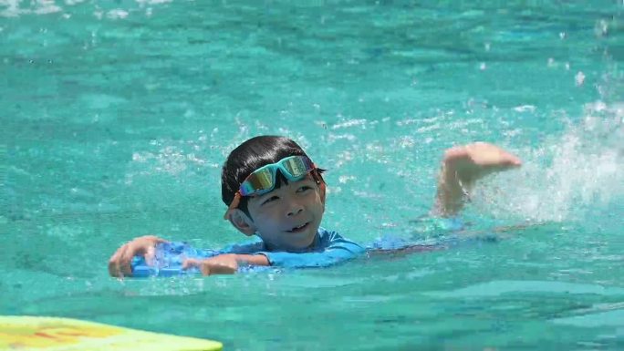 一个男孩戴着泳镜漂浮在泳池上，慢镜头