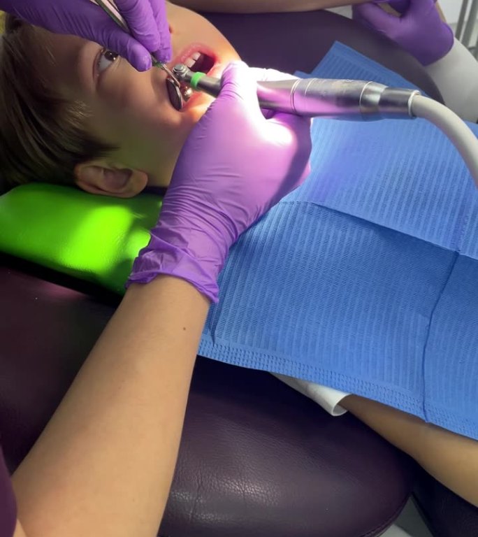 一位戴着医用口罩和紫色橡胶手套的牙医给一个蹒跚学步的小男孩戴上了印章。牙科治疗、检查、小儿牙科。专业