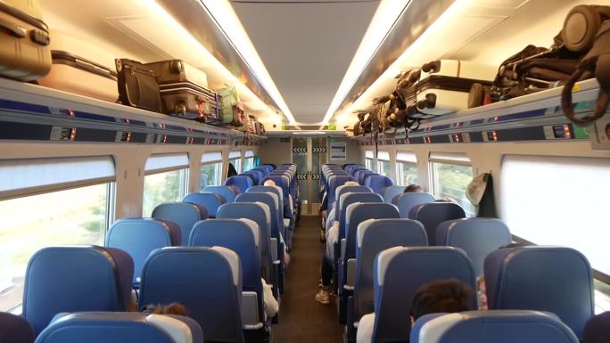 一辆移动的火车车厢的内部视图，乘客坐着，行李放在架子上