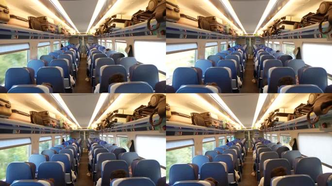 一辆移动的火车车厢的内部视图，乘客坐着，行李放在架子上