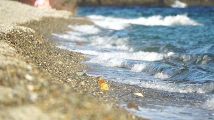 小海浪，模糊的软泡沫海浪冲刷金色卵石沙滩夕阳。海滩上的海浪。没有人。假日休闲概念。抽象航海夏季海洋日