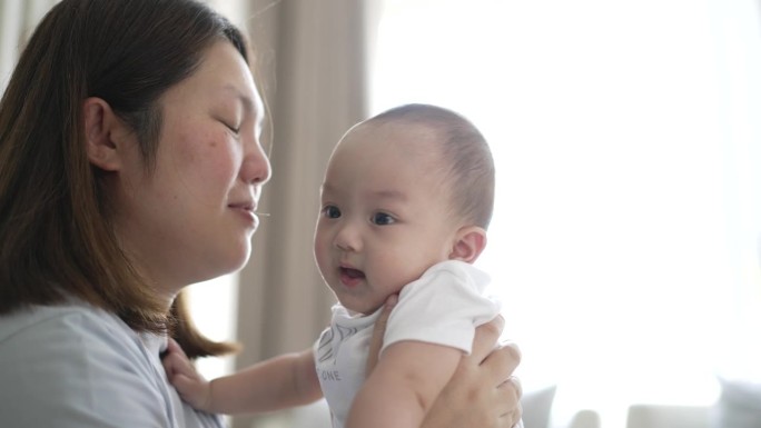 幸福的母子在家里亲吻并将男婴抛向空中