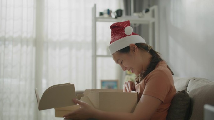 快乐的亚洲女人在圣诞节在家打开盒子