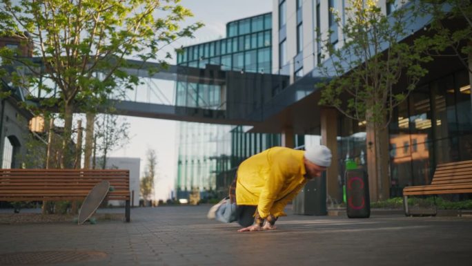 年轻而健壮的B-Boy在现代建筑之间的城市街道上独自用扬声器打破节拍。为即将到来的霹雳舞比赛练习自由