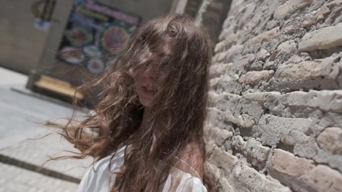 一位年轻女子，一头飘逸的长发，身穿浅白色背心裙，站在一座东方城市的古城墙旁