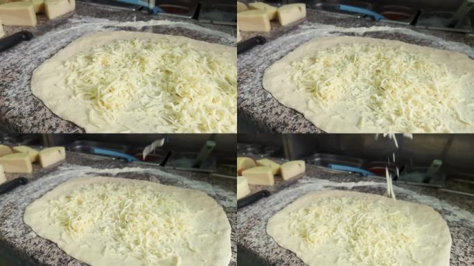 把新鲜磨碎的奶酪撒在披萨面团上，近距离。