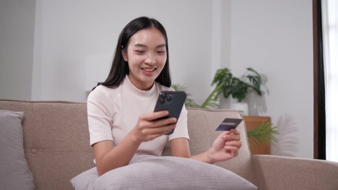 年轻的亚洲女性在家里用信用卡和手机网购。