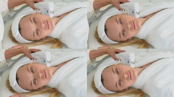 漂亮的女性客户穿着浴袍躺在美容床上的脸部特写，用超声波装置进行颈部提拉手术。