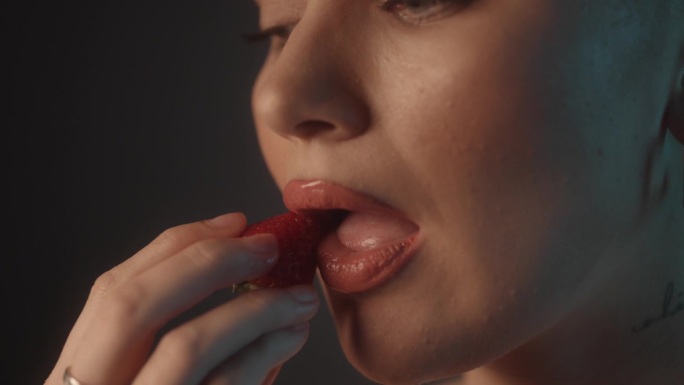 美丽性感的女人用红色的口红把草莓压在她的嘴唇上，然后咬一口