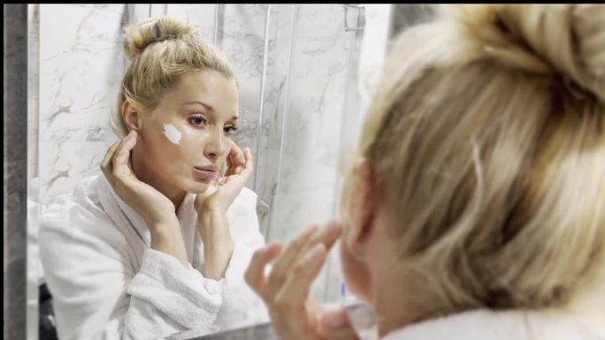 女人在浴室里照镜子，照顾自己的皮肤。