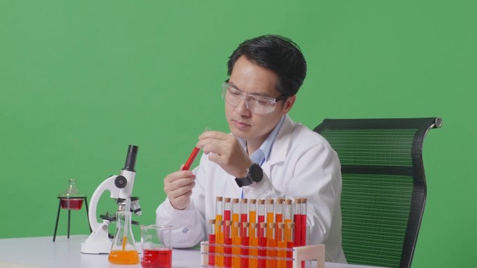 侧视图:在绿屏背景的实验室里，亚洲男性科学家用显微镜看着试管里的红色液体，在桌子上摇头