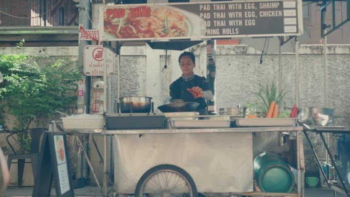 泰国美食:女厨师在繁华的曼谷街头市场炒制美味的泰式炒粉。