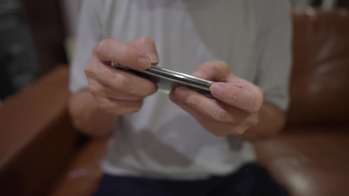 一名男子坐在沙发上用手机玩在线社交媒体游戏，近距离观察他的双手