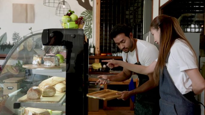 亚洲咖啡店老板帮助印度丈夫把面包从橱柜里拿出来。谁来买他家族的小生意——咖啡店