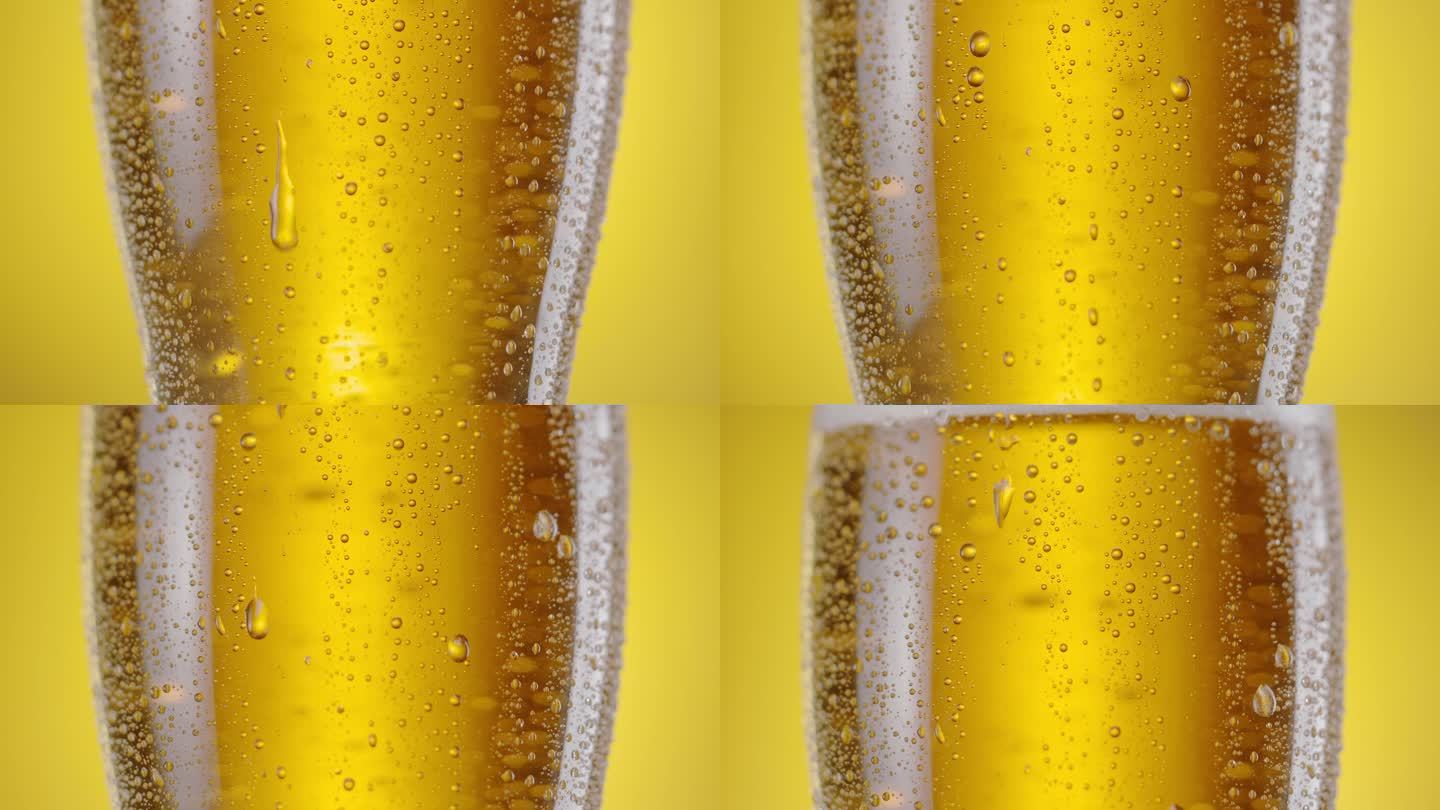 摄像机沿着装有淡啤酒的啤酒杯缓缓升起。玻璃上有很多水珠，上面还有啤酒泡沫。黄色背景。