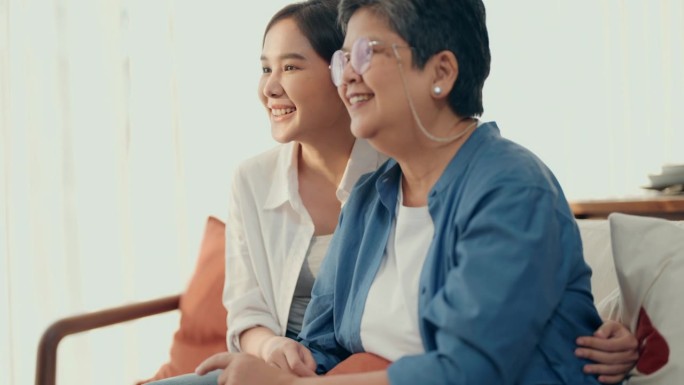 在家的美好时光:亚洲老年妇女和女儿一起看电视，充满了快乐和交谈