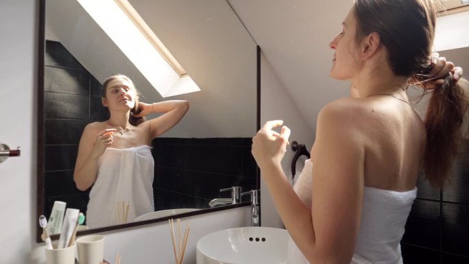 一个女人站在浴池里，用毛巾盖着，凝视着镜子里的自己。良好的卫生习惯和自我保健习惯