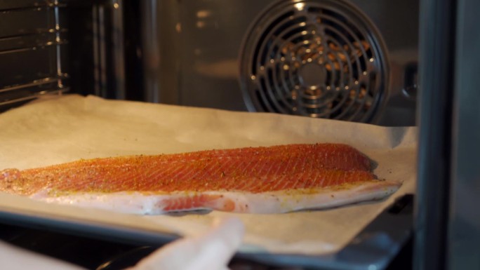 烹饪烤鱼的妇女把装有鳟鱼的烤盘放进热烘烘的电烤箱