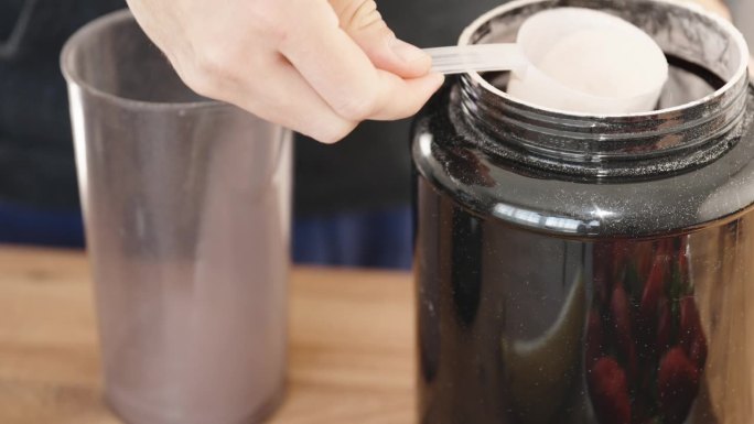 运动蛋白饮料，用量勺把粉末倒进杯子里，特写。
