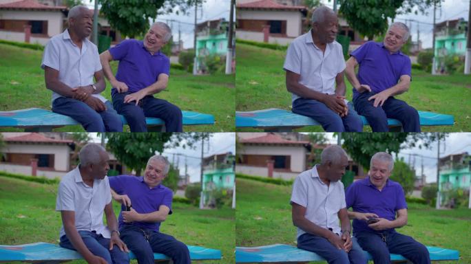 一位老人在户外公园的长椅上和老人聊天时掏出手机。快乐多元友谊互动，巴西老年人关系，查看手机