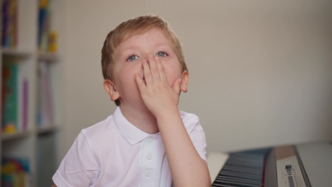 奇怪的蹒跚学步的孩子舔着手掌，在钢琴旁看着手