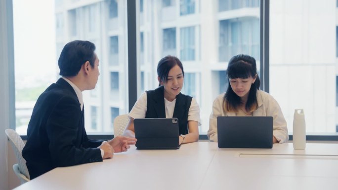 亚洲商人在现代办公空间与同事们指着屏幕交谈。
