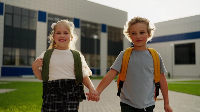 欢快的一年级男孩和女孩背着书包在操场上散步，孩子们的肖像