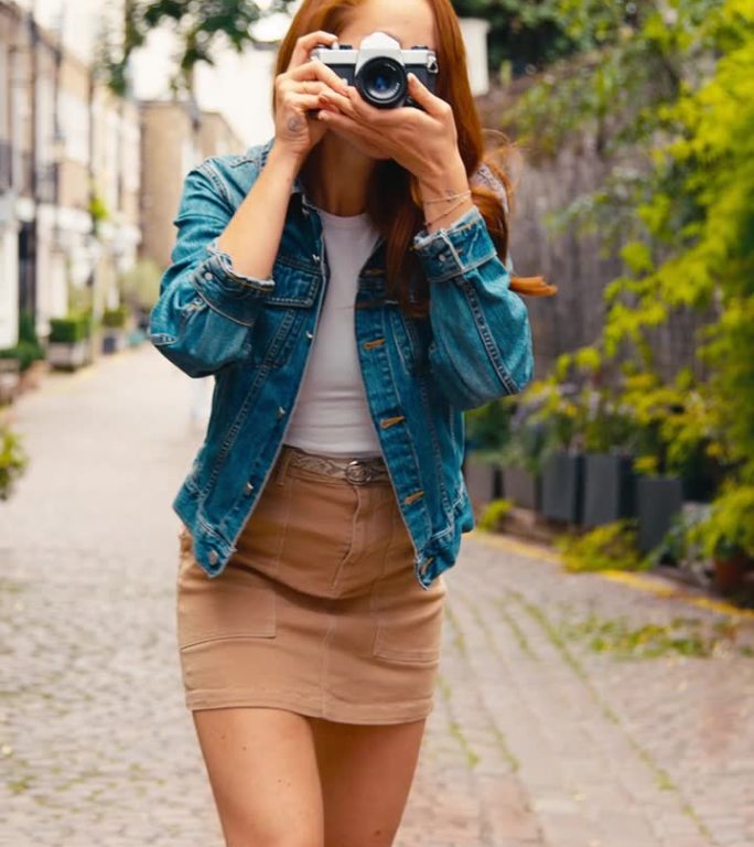 城市里年轻女子用数码相机拍照的垂直视频发布到社交媒体上