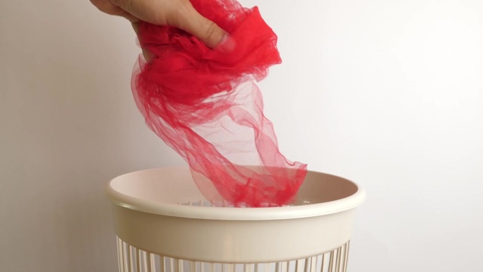 一块红色的织物被回收后扔进了垃圾桶。废物处理和回收的概念。