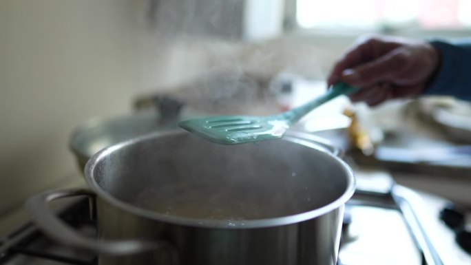 近距离用手检查金属锅里的意大利面，以确保它有嚼劲。在厨房炉子上烹调碳水化合物食物的程序