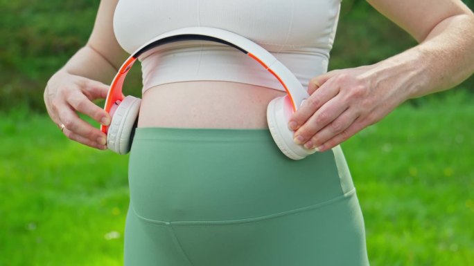 孕妇把耳机夹在肚子上。怀孕的概念。