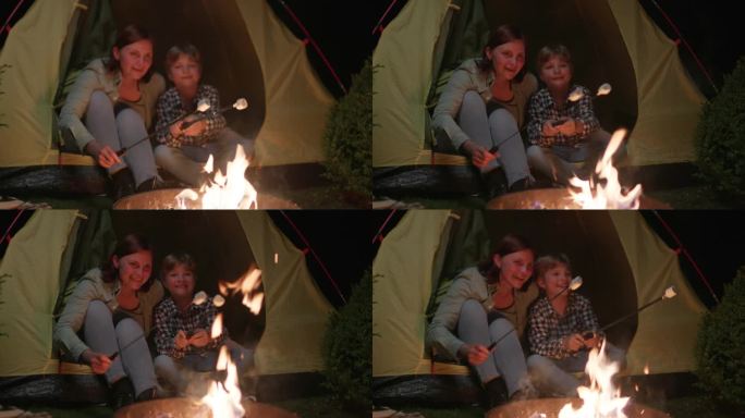 妈妈和儿子晚上在篝火上烤棉花糖。一家人在火堆旁露营。