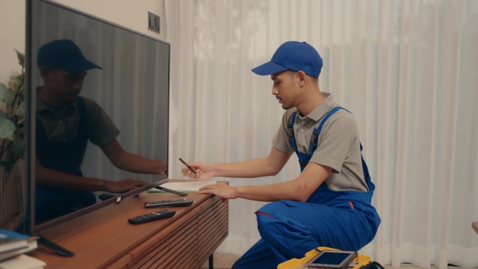穿着蓝色连衣裤的熟练亚洲男工人熟练地修理大型电视-专业的电子维修服务