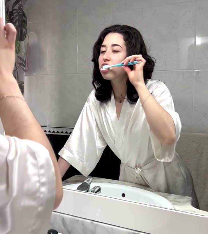 年轻女子在镜子前刷牙的垂直视频。对着浴室镜子刷牙的快乐女人