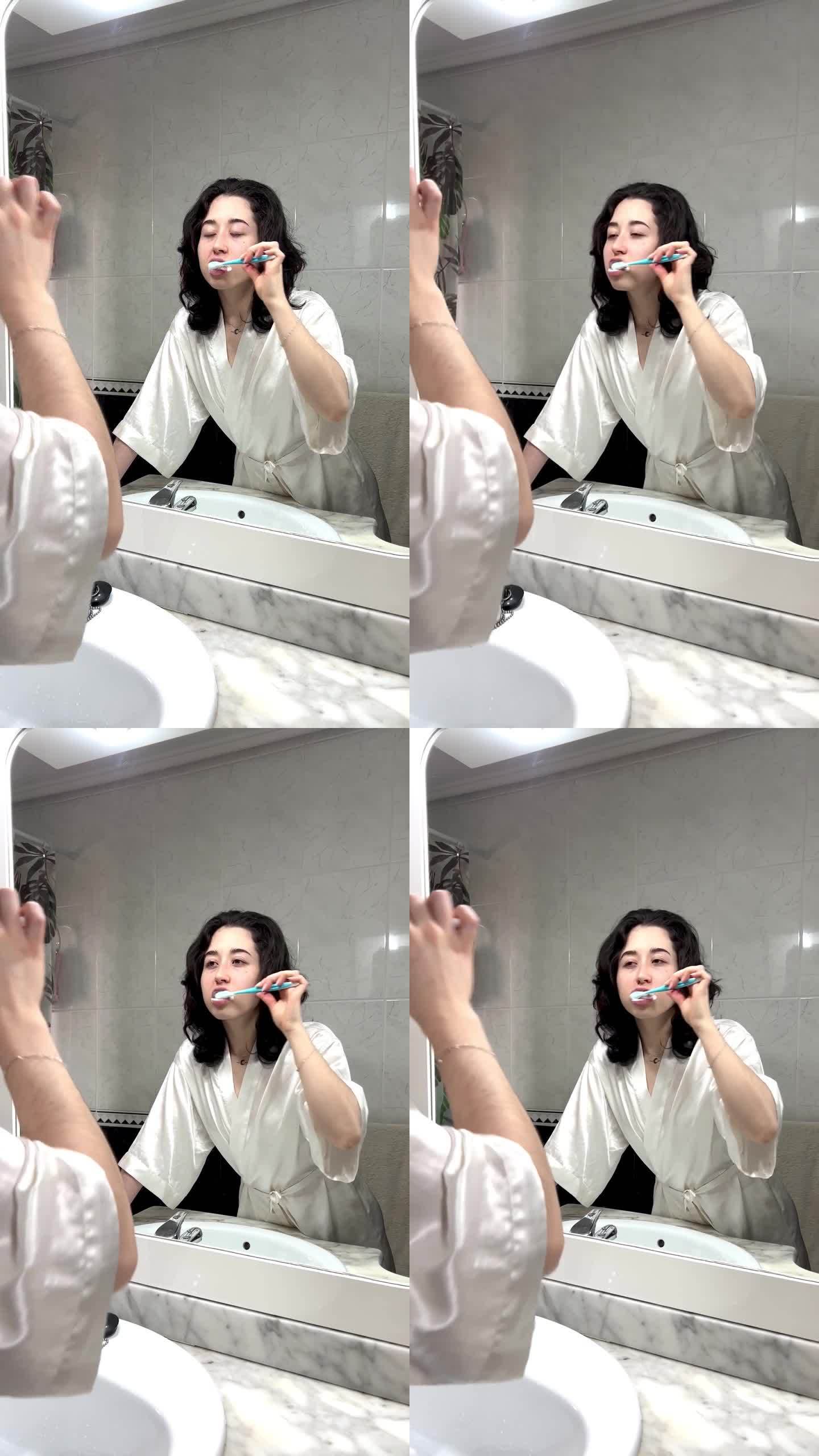 年轻女子在镜子前刷牙的垂直视频。对着浴室镜子刷牙的快乐女人