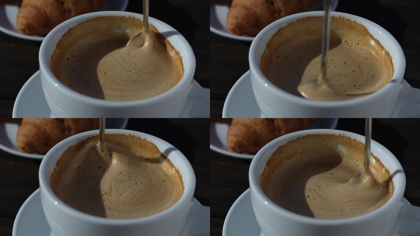 用勺子在白色杯子里搅拌热咖啡卡布奇诺的浓泡沫
