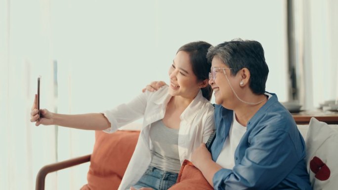 代际连接:亚洲老年妇女和女儿的快乐时刻，在看电视时分享笑声和正能量