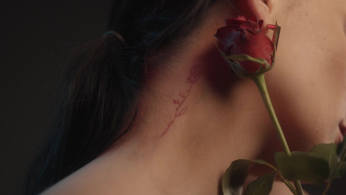 性感的女人用红色的口红和玫瑰纹身黑色背景工作室拍摄的摆姿势与一个单一的红玫瑰和调情的相机