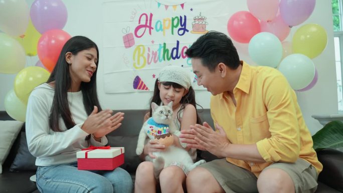 为了庆祝他们的小白猫的生日，一个亚洲家庭，印度中年母亲，亚洲父亲和6岁的女儿准备了一个美丽的背景来庆