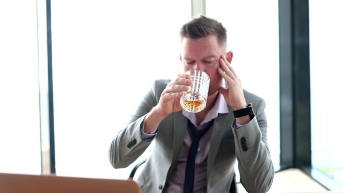 穿着西装的醉醺醺的商人在笔记本电脑前喝着玻璃杯里的威士忌，看着4k慢动作电影