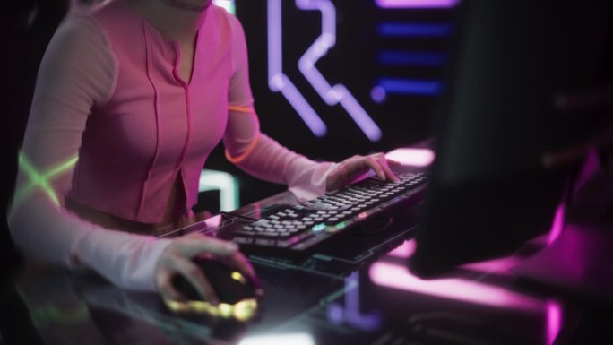 年轻女性在台式电脑上玩在线视频游戏。游戏女孩坐在交互式数字桌子后面，从未来主义的霓虹灯房间流媒体游戏