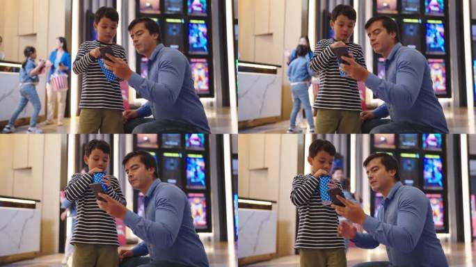 亚洲父亲和小儿子在电影院用智能手机购买电影票。父子俩周末一起在电影院通过智能手机预订座位。家庭活动概